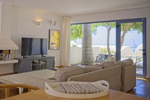 A living room with a television, sofa, and a view of the sea.