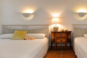 A hotel room with two beds, a nightstand with a lamp, and wall sconces.