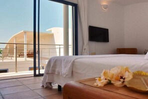 Ein Hotelzimmer mit einem Bett, einem Flachbildfernseher und Blick auf ein Gebäude durch ein großes Fenster.