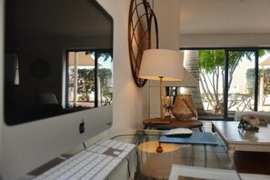 Ein stilvolles Zimmer mit Schreibtisch, Computer, Lampe und großen Fenstern.