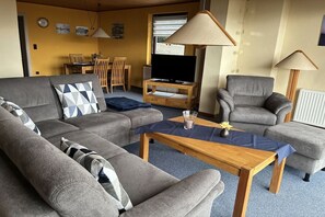 A living room with a sofa, armchairs, a coffee table, a TV, and a dining area in the background. - Holiday apartment with 2 bedrooms (St. Andreasberg)