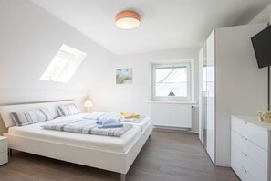 Un dormitorio con cama, mesitas de noche, una ventana, un radiador y un televisor.