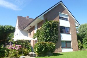 Ein zweistöckiges Haus mit Ziegelaußenwand, geneigtem Dach und einem Garten mit rosa Blumen.