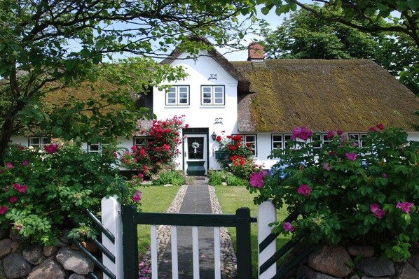 A traditional white cottage with a thatched roof, numbered 27, surrounded by lush greenery and flowering plants. - Keitumer Chaussee 5 Holiday Apartment 1 (Westerland)