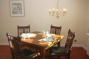 A dining room with a wooden table set for four, surrounded by chairs, a chandelier, and a framed picture on the wall. - Keitumer Chaussee 5 Holiday Apartment 1 (Westerland)