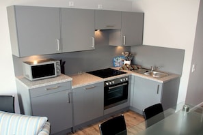 A compact kitchen with grey cabinets, a microwave, a stove, and a sink. - Holiday apartment in Sylt with 3 bedrooms (Westerland)