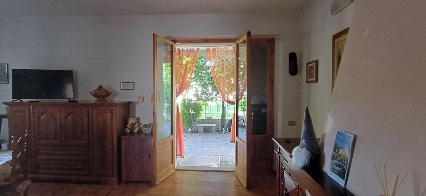 An open doorway leading to an outdoor area with a bench, a television on a cabinet, and a framed picture on the wall.