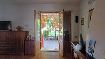 An open doorway leading to an outdoor area with a bench, a television on a cabinet, and a framed picture on the wall.