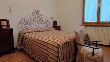 A bedroom with a bed, a chair, a nightstand, a lamp, a decorative headboard, and a window with curtains.