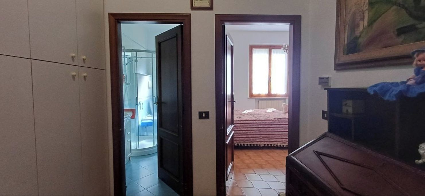 Ein Flur, der zu einem Schlafzimmer führt, mit einem Bett, einer Kommode und einem Gemälde an der Wand.