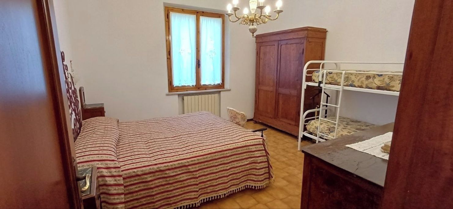 A room with a bunk bed, a wooden wardrobe, a radiator, and a window with curtains.