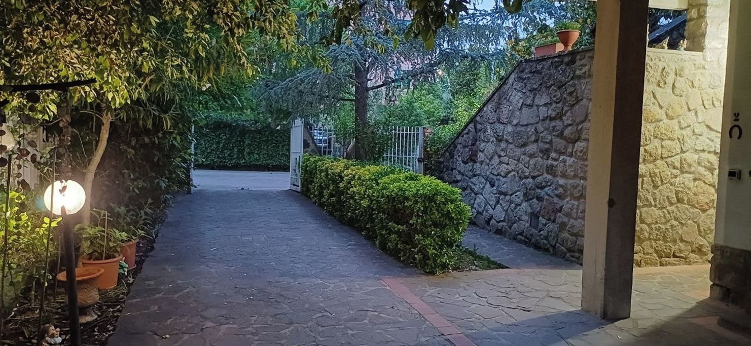 Un sendero pavimentado que conduce a la entrada de un edificio, bordeado por vegetación y muros de piedra.