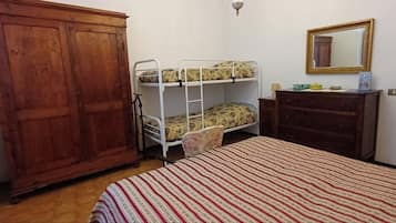A room with a bunk bed, a wooden wardrobe, a dresser, and a mirror on the wall.