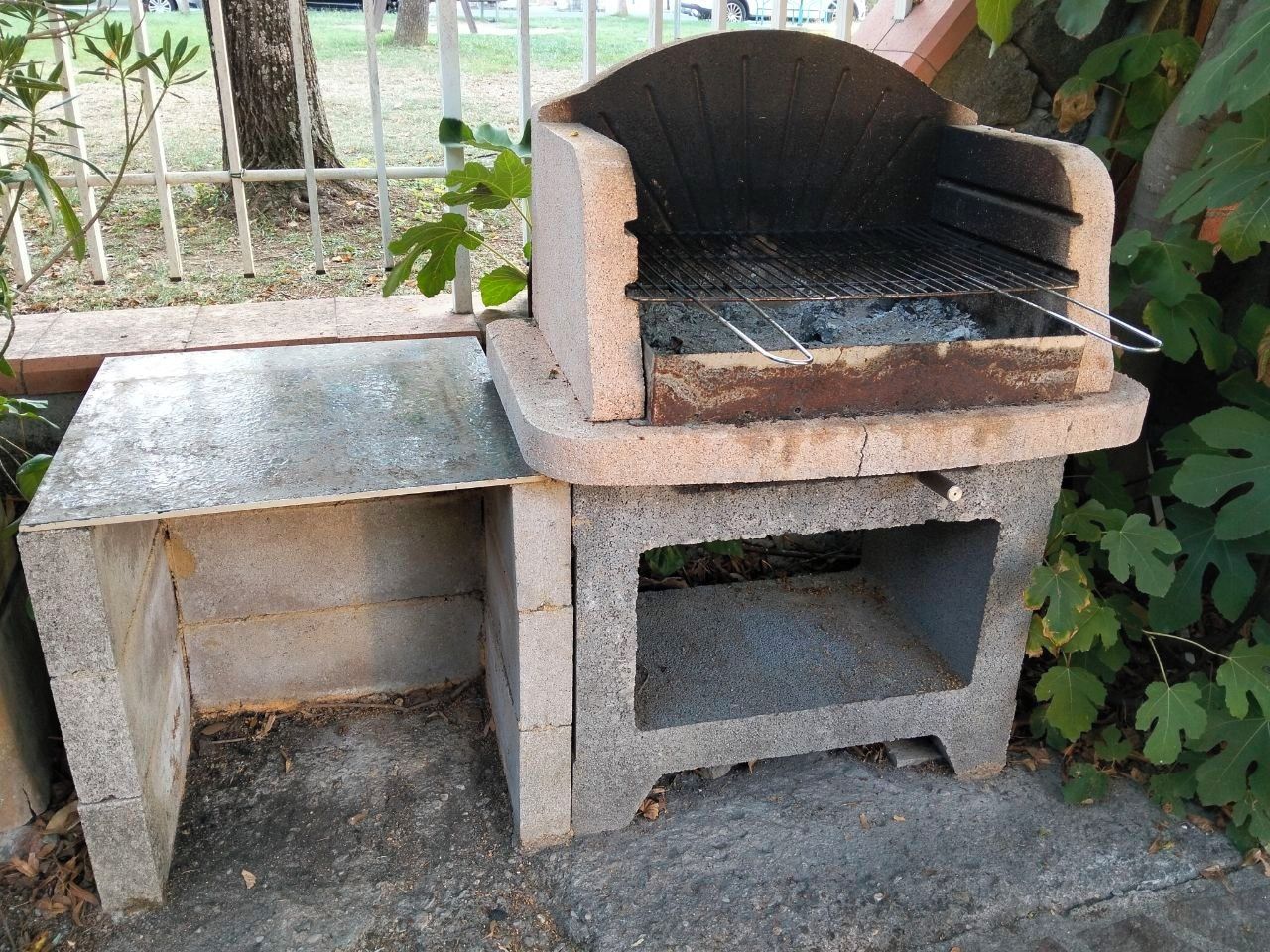 A concrete outdoor grill with a metal grate and a metal handle.