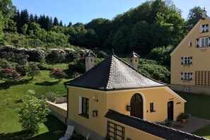 A two-story building with a tiled roof, a small balcony, and a garden with shrubs and flowers. - Klingenburger bakery (Jettingen-Scheppach)