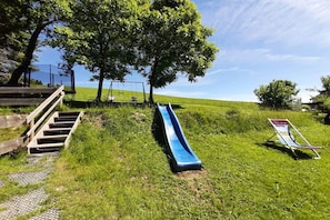 A grassy area with a blue slide, a metal bench, and a staircase leading up. - Guesthouse Schmid & Reitzner 2 (Immenstadt)