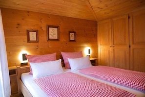 A wooden-paneled room with two beds, each with a checkered bedspread and white pillows. There are framed pictures on the wall and a wooden wardrobe. - Guesthouse Schmid & Reitzner 2 (Immenstadt)