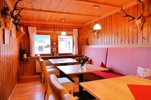 Interior acogedor de una cabaña con paredes de madera, una zona de comedor y un rincón de estar con un cojín rosa.