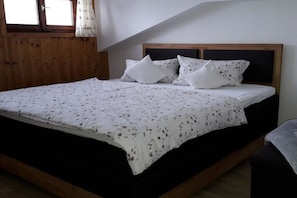 A bedroom with a wooden headboard, a bed with a floral bedspread, and a window with curtains. - Guesthouse Schmid & Reitzner 2 (Immenstadt)