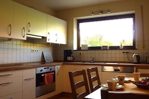 Eine Küche mit weißen Schränken, einem Fenster mit Blick und einem Tisch mit Tassen und einem Wasserkocher.
