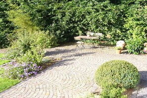 A paved garden area with a circular brick pattern, a wooden table with chairs, and a potted plant. - Holiday apartment with 2 bedrooms (Schwirzheim)
