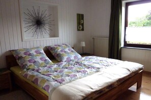 A bedroom with a bed, a wall clock, a radiator, and a window with curtains. - Holiday apartment with 2 bedrooms (Schwirzheim)