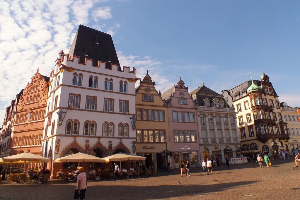 A historic European square with traditional architecture, outdoor seating, and a cobblestone ground.