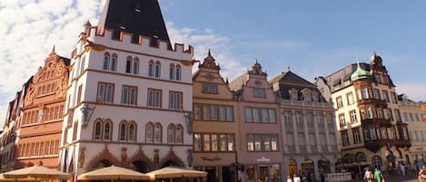 A historic European square with traditional architecture, outdoor seating, and a cobblestone ground.