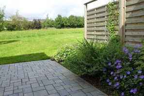 A paved pathway leading to a grassy area with a wooden fence and flowering plants. - Holiday apartment with 2 bedrooms (Schwirzheim)