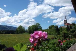 A church with a bell tower, surrounded by a garden with flowers and a field in the background. - Guesthouse Schmid & Reitzner 3 (Immenstadt)