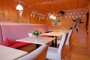 Een restaurant met houten wanden, een rode gewatteerde bank, witte tafels en stoelen.