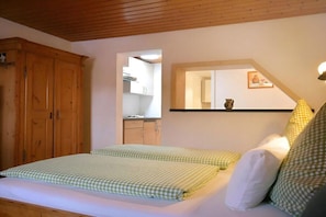 A bedroom with a bed, wooden wardrobe, and a mirror reflecting a kitchen area. - Guesthouse Schmid & Reitzner 3 (Immenstadt)