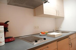 A kitchen with a built-in induction cooktop, a red electric kettle, a sink with a faucet, and wooden cabinets. - Guesthouse Schmid & Reitzner 3 (Immenstadt)