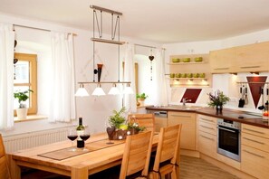 A modern kitchen with wooden cabinets, a built-in oven, and a dining area with a wooden table and chairs. - on the farm Trout Riding Stable (Neureichenau)