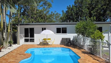 Ein Swimmingpool mit weißem Zaun, eine Terrasse mit Stühlen und ein Gebäude mit Fenstern.