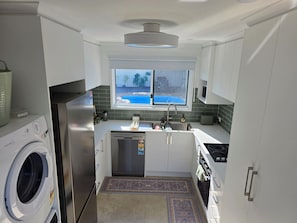 Een praktische keuken met een geïntegreerde wasmachine, een vaatwasser en een raam met uitzicht op een achtertuin.