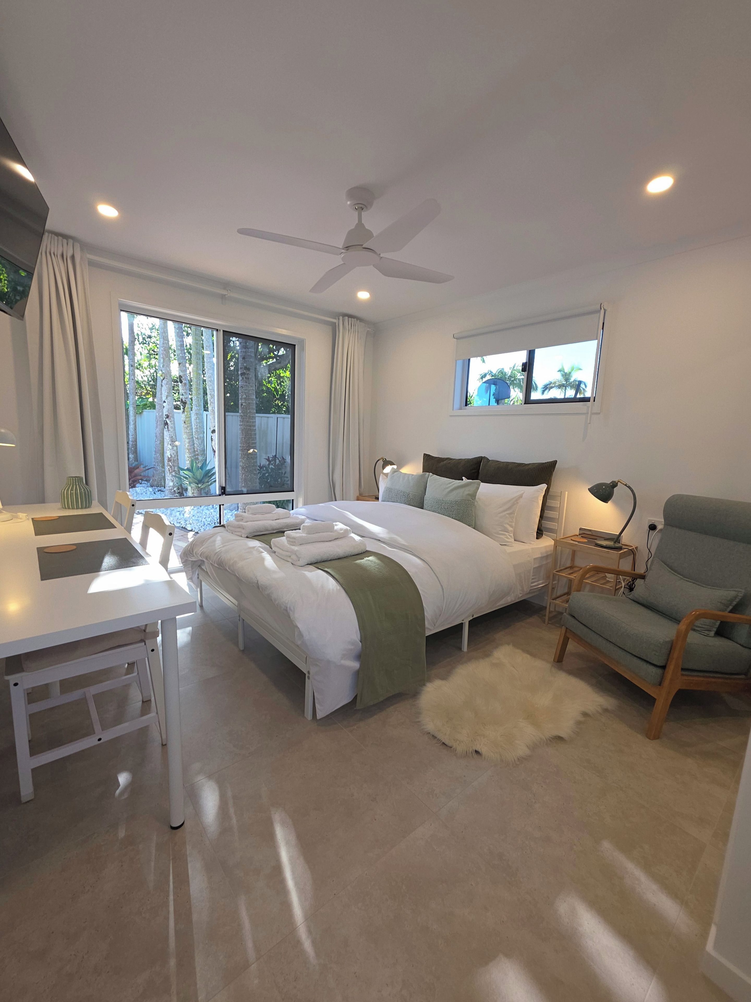 A bedroom with a bed, bedside table, chair, and a window with curtains.