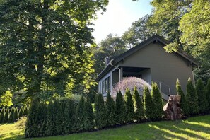 Ein Wohnhaus mit geneigtem Dach, einer Veranda und einem gepflegten Garten mit verschiedenen Sträuchern und einem Baumstumpf.
