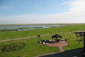 A grassy area with a covered pavilion, a small body of water, and a distant view of a flat landscape. - Holiday apartment with 1 bedroom (Carolinensiel)