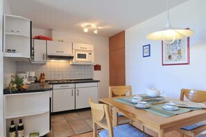 Une cuisine compacte avec des meubles blancs, un four à micro-ondes et un coin repas avec une table dressée pour deux personnes.