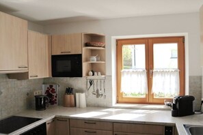 A kitchen with a built-in microwave, a coffee machine, and a window with curtains. - Holiday apartment with 1 bedroom (Hopfen am See)