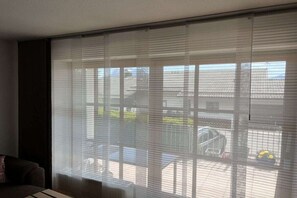 A room with a large window covered by blinds, a sofa, and a table. - Holiday apartment with 1 bedroom (Hopfen am See)