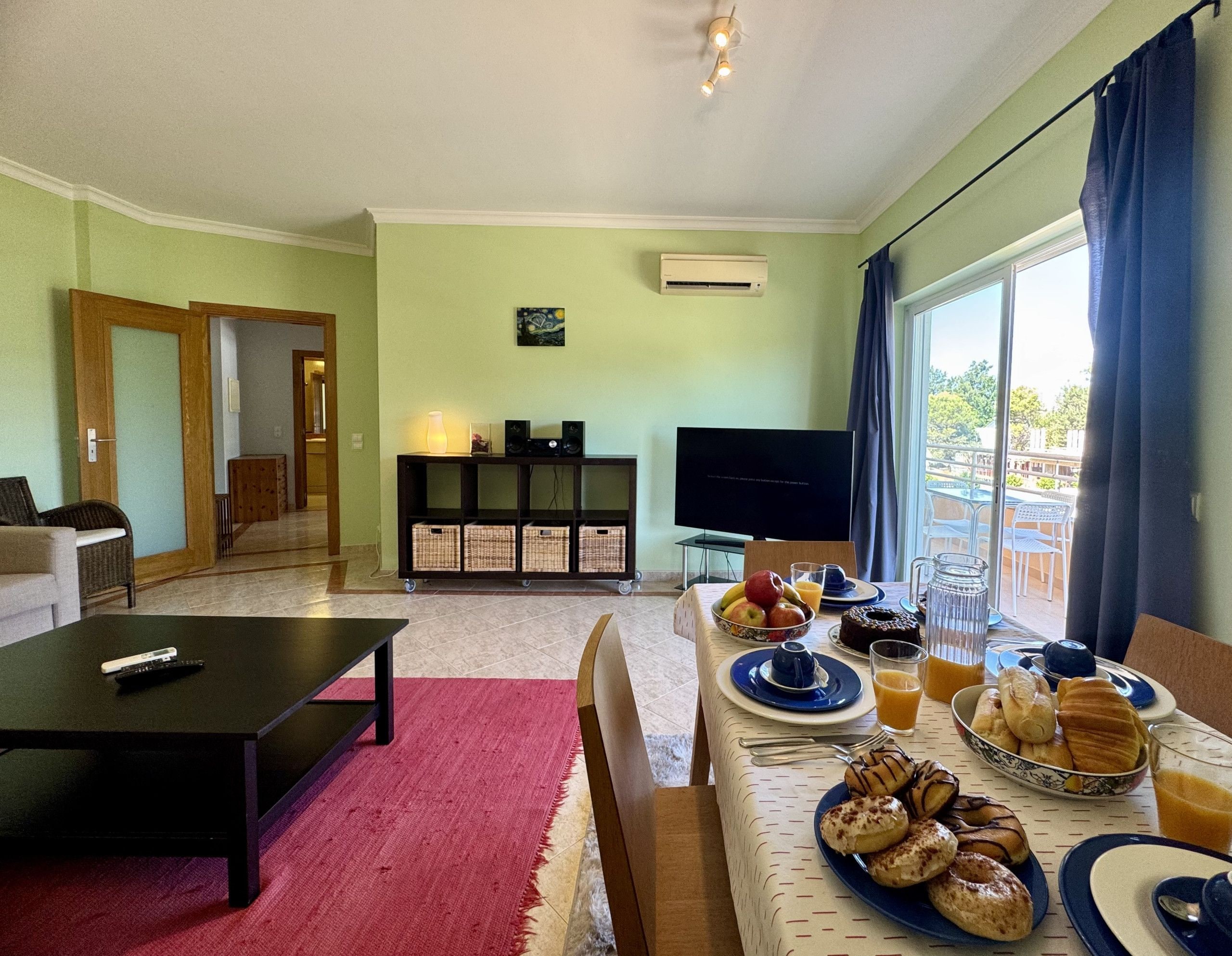 Een woonkamer met een televisie, een ontbijt gedekte eettafel en uitzicht op de omgeving.