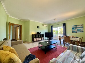 A living room with a sofa, a coffee table, a TV, and a dining area with a table and chairs. - Vilamoura Typical 5 With Pool by Homing (Loulé)