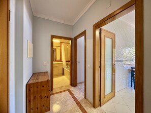 Ein Flur mit Holztüren, der zu einem Badezimmer und einem Raum mit rauen Glasswänden führt.