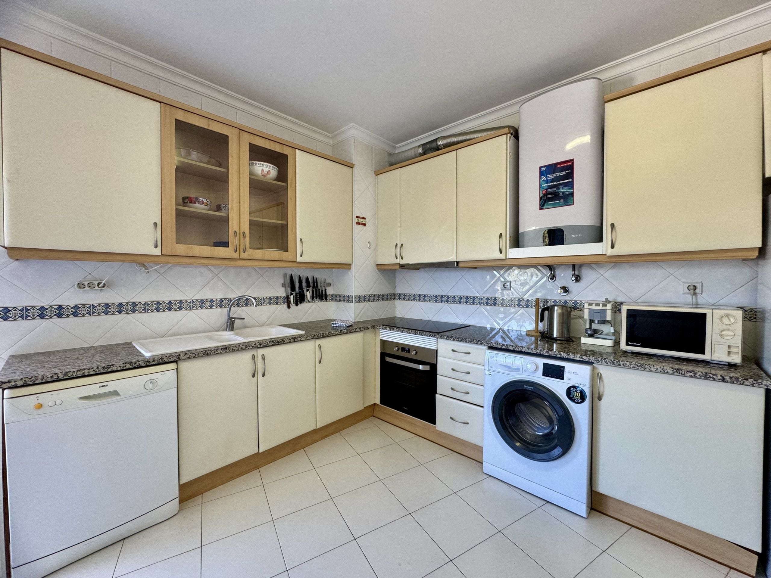 Een kleine keuken met een wasmachine, magnetron, spoelbak en kastjes.
