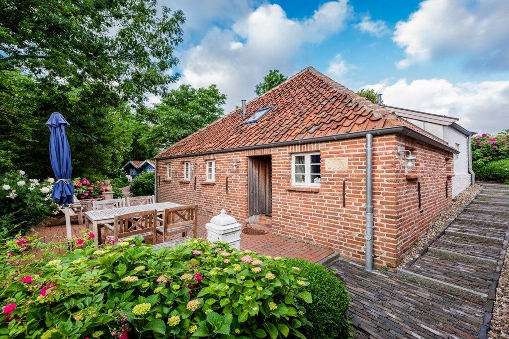 A brick house with a tiled roof, a wooden deck, and a garden with flowers and shrubs.