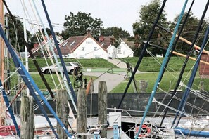 Ein Yachthafen mit vertäuten Booten, ein weißes Gebäude mit rotem Dach im Hintergrund und ein Auto auf der Straße geparkt.