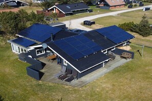 Ein Wohngebäude mit einer großen Solaranlage auf dem Dach, einer überdachten Terrasse mit Sitzgelegenheiten und einer Garage.