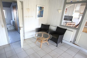 Ein Zimmer mit einem Glastisch, zwei schwarzen Stühlen, einem Korbstuhl, einem Bild an der Wand und einem Spiegel, der den Raum reflektiert.